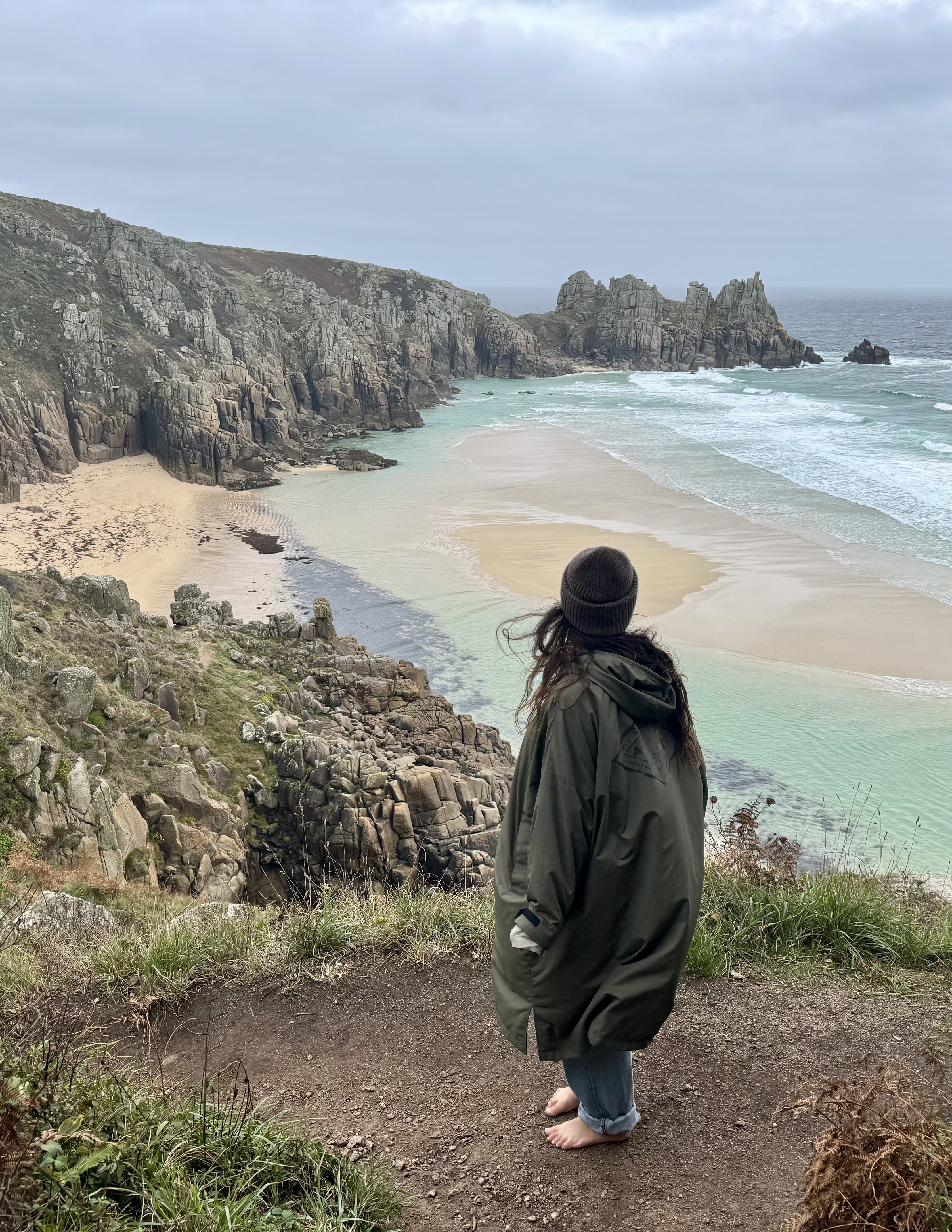 A person standing near cliffs above a quiet beach and ocean