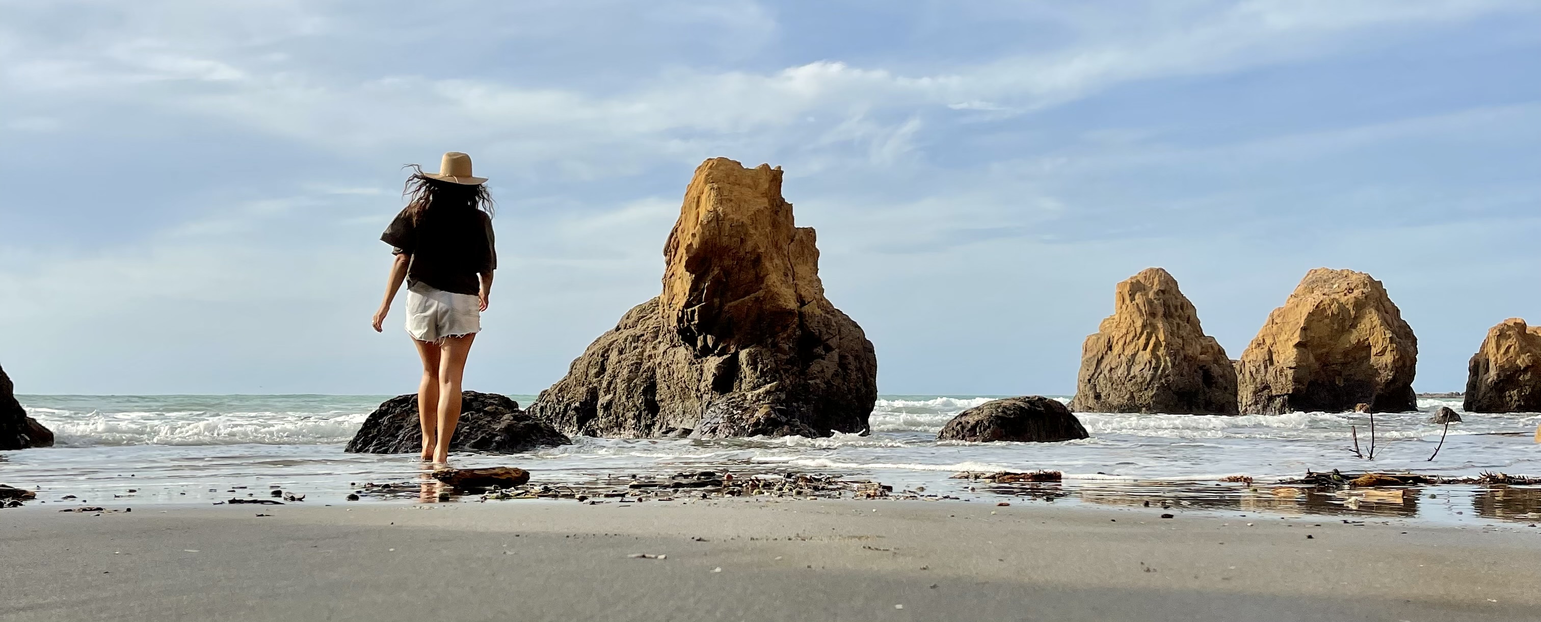 A quiet beach scene with a person walking toward ocean rocks